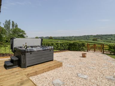 An outdoor area with a hot tub on a wooden platform and a gravel ground with stepping stones and a wooden gate at The Shippon in Honiton