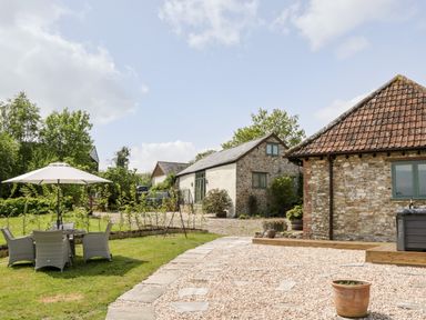 A garden with outdoor seating and umbrella next to stone buildings at The Shippon in Honiton