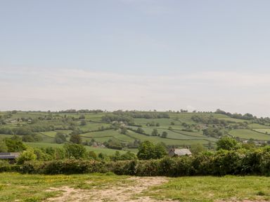 A rural landscape with green fields trees and houses under a clear sky at The Shippon in Honiton