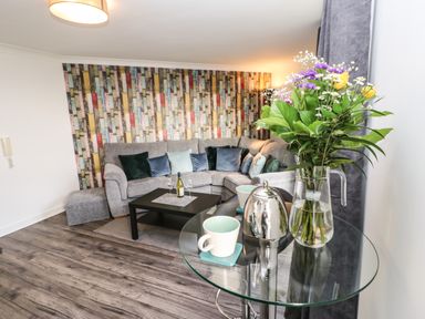 A living room with a grey sofa and colorful wallpaper at Sandy Corner in Blyth Northumberland