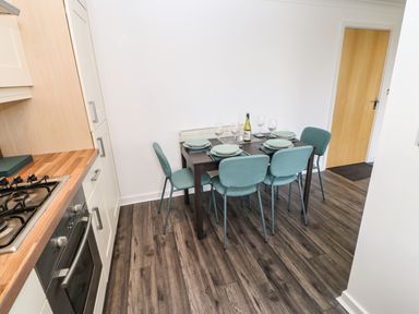 A kitchen dining area with a dark wood table set for six people with green chairs and a bottle on the table at Sandy Corner in Blyth Northumberland