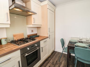 A kitchen with a gas stove oven wooden countertop green canisters and a dining table set with plates and wine glasses at Sandy Corner in Blyth Northumberland