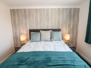 A bedroom with a bed with three pillows and a turquoise blanket with two bedside tables with lamps at Sandy Corner in Blyth Northumberland