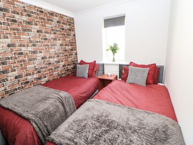 A bedroom with two single beds with red bedding and grey throws and a brick accent wall at Sandy Corner in Blyth Northumberland