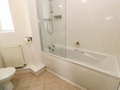 A bathroom with a bathtub shower combination a toilet radiator and tiled floor at Sandy Corner in Blyth Northumberland
