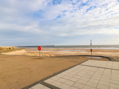 A beach with sand and sea viewed from a paved promenade with a lifebuoy and a signpost at Sandy Corner in Blyth Northumberland
