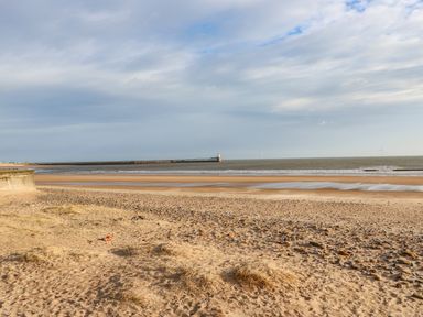A sandy beach with scattered rocks and a pier with a lighthouse in the distance at Sandy Corner in Blyth Northumberland