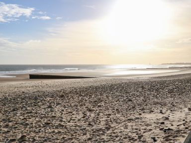 A sandy beach with scattered rocks and a sea wall under a bright sky at Sandy Corner in Blyth Northumberland