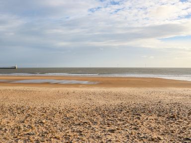 A sandy and rocky beach with a lighthouse on the left and wind turbines in the distance at Sandy Corner in Blyth Northumberland