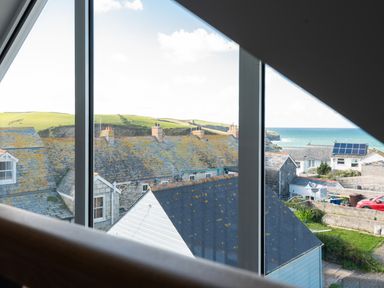 A view of rooftops hills and the sea through a window at Church Rooms in Port Isaac