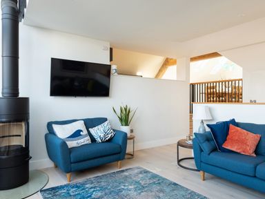 A living room with blue sofas a wall-mounted television and a round black stove at Church Rooms in Port Isaac