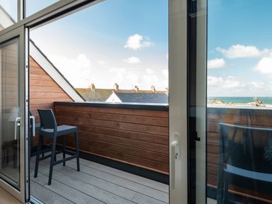 A balcony with a high chair and wooden railing overlooking rooftops and the sea at Church Rooms in Port Isaac
