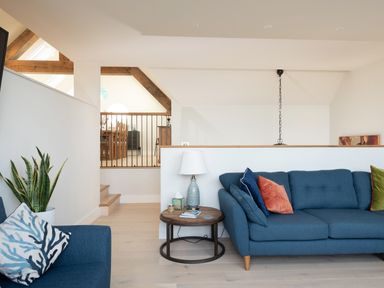 A living area with a blue sofa and cushions a round wooden side table with a lamp and a plant in a white pot at Church Rooms in Port Isaac