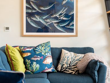 A blue sofa with colorful pillows and a fish painting on the wall at Church Rooms in Port Isaac