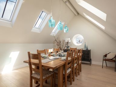 A dining room with a wooden table and chairs under skylights and blue pendant lights at Church Rooms in Port Isaac