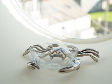 A decorative glass bowl with silver crab-shaped metal legs on a white surface by a round window at Church Rooms in Port Isaac