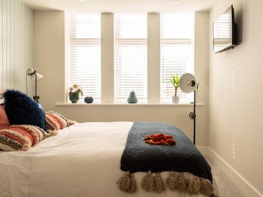 A bedroom with a bed near three windows with blinds and decorative items on the windowsill at Church Rooms in Port Isaac