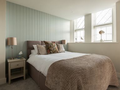 A bedroom with a bed pillows blanket bedside tables lamps and decorative items on the windowsill at Church Rooms in Port Isaac