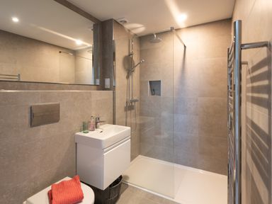 A bathroom with a shower area a white sink and toilet with a red towel on it at Church Rooms in Port Isaac