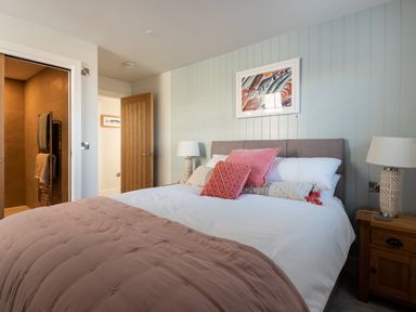 A bedroom with a bed with pink and white pillows a bedside table with a lamp a wooden door and a bathroom door at Church Rooms in Port Isaac
