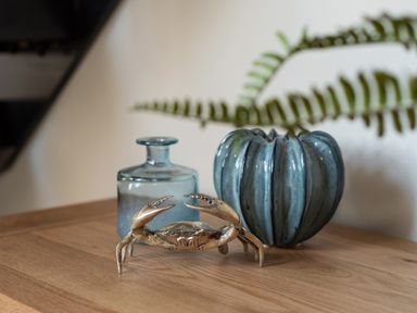 A wooden surface with a brass crab sculpture a blue glass bottle and a blue ceramic vase with a fern at Church Rooms in Port Isaac