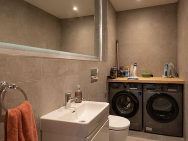 A laundry room with a sink washing machine dryer and cleaning supplies at Church Rooms in Port Isaac