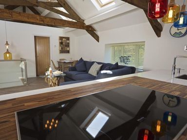 A kitchen with a wooden countertop and hob overlooking a living area with a blue couch and wooden beams at The Barn 20 At The Beach Torcross
