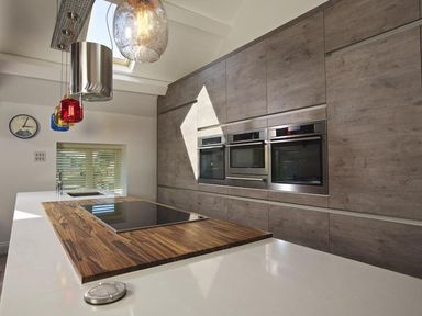 A kitchen with built in ovens wooden countertop and colorful pendant lights at The Barn 20 At The Beach Torcross