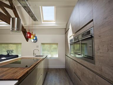 A kitchen with wooden cabinets a wooden countertop an induction cooktop a sink three colored pendant lights and skylight windows at The Barn 20 At The Beach in Torcross
