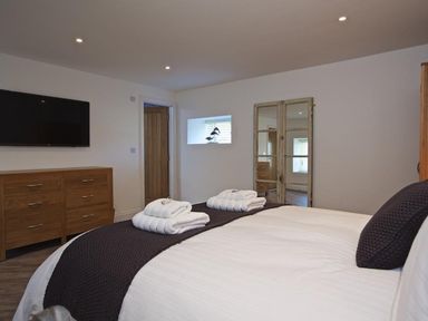 A bedroom with a bed folded towels a wooden dresser a wall-mounted TV and a mirror at The Barn 20 At The Beach Torcross
