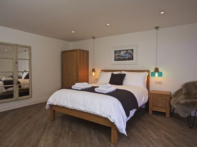 A bedroom with a wooden bed white bedding bedside table wardrobe and a chair with a fur throw at The Barn 20 At The Beach Torcross