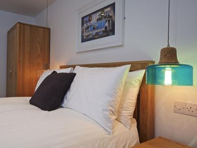 A bedroom with a wooden bedframe white pillows a black cushion a blue hanging lamp and a wooden wardrobe at The Barn 20 At The Beach Torcross