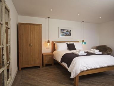 A bedroom with a wooden bed with white bedding and dark pillows wooden wardrobe and nightstand with hanging pendant lights at The Barn 20 At The Beach in Torcross