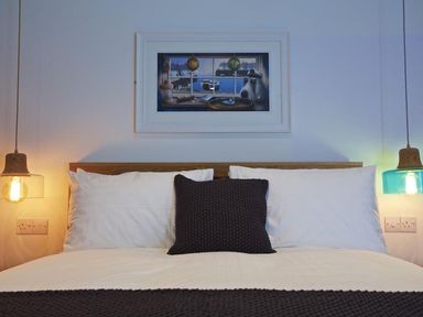 A bed with pillows and a knitted blanket with pendant lights and a framed picture above at The Barn 20 At The Beach in Torcross