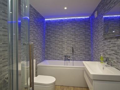 A bathroom with a bathtub toilet and sink with blue lighting on the tiled walls at The Barn 20 At The Beach Torcross