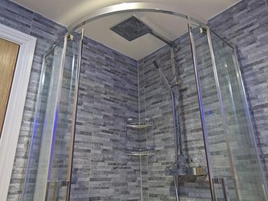 A shower area with glass doors grey tiled walls and a metal shower fixture at The Barn 20 At The Beach Torcross