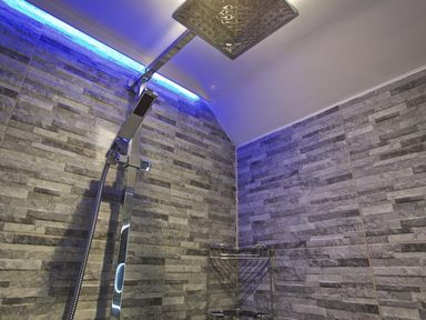 A shower area with a rainfall showerhead and handheld shower on tiled walls with blue LED lighting at The Barn 20 At The Beach in Torcross