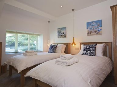 A bedroom with two single beds white bedding and pillows towels hanging lights and window blinds at The Barn 20 At The Beach in Torcross