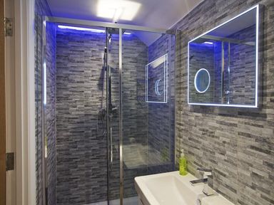 A bathroom with a glass shower enclosure a sink with a faucet and a backlit mirror at The Barn 20 At The Beach Torcross