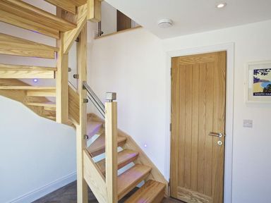 A wooden staircase next to a wooden door in a white hallway at The Barn 20 At The Beach Torcross