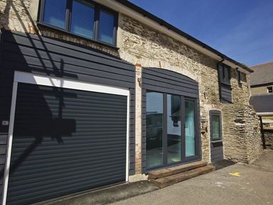Exterior of a stone and wood building with a garage door and glass entrance at The Barn 20 At The Beach Torcross