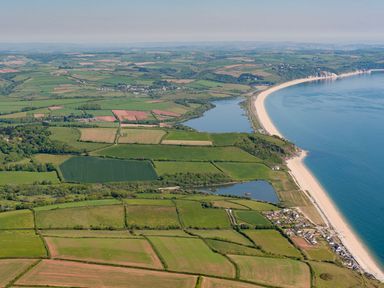 An aerial view of fields lakes a curved sandy beach and a coastal village at The Barn 20 At The Beach in Torcross