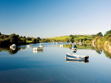 A river with boats floating on the water and grassy hills in the background at The Barn 20 At The Beach in Torcross