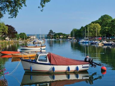 A river with several boats moored on both sides and trees along the banks at The Barn 20 At The Beach in Torcross