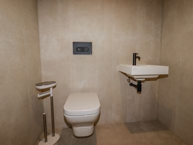 A bathroom with a wall-mounted toilet a floating sink with a black faucet and a toilet paper holder at 13 Cliff Edge in Newquay