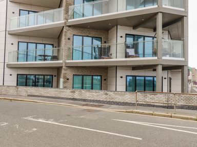 A modern apartment building with glass balconies and outdoor furniture on some balconies in Newquay