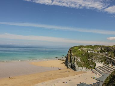 A beach with sand and cliffs and people on the sand and buildings near the cliffs at 13 Cliff Edge in Newquay