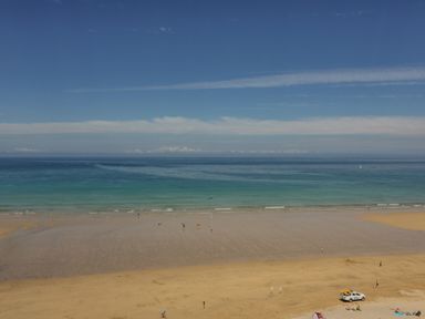 A beach with people on the sand and in shallow water and a rescue vehicle on the shore at 13 Cliff Edge in Newquay