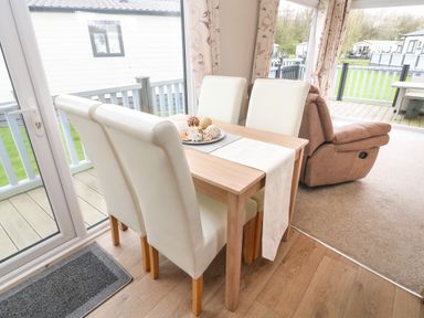 A dining area with a wooden table and four white chairs next to glass doors leading to a deck at Yealands 27 South Lakeland Leisure Village near Carnforth