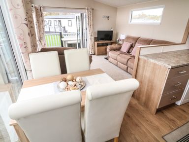 A dining table with four chairs and decorative balls on the table next to a living area with two brown sofas and a TV at Yealands 27 South Lakeland Leisure Village near Carnforth